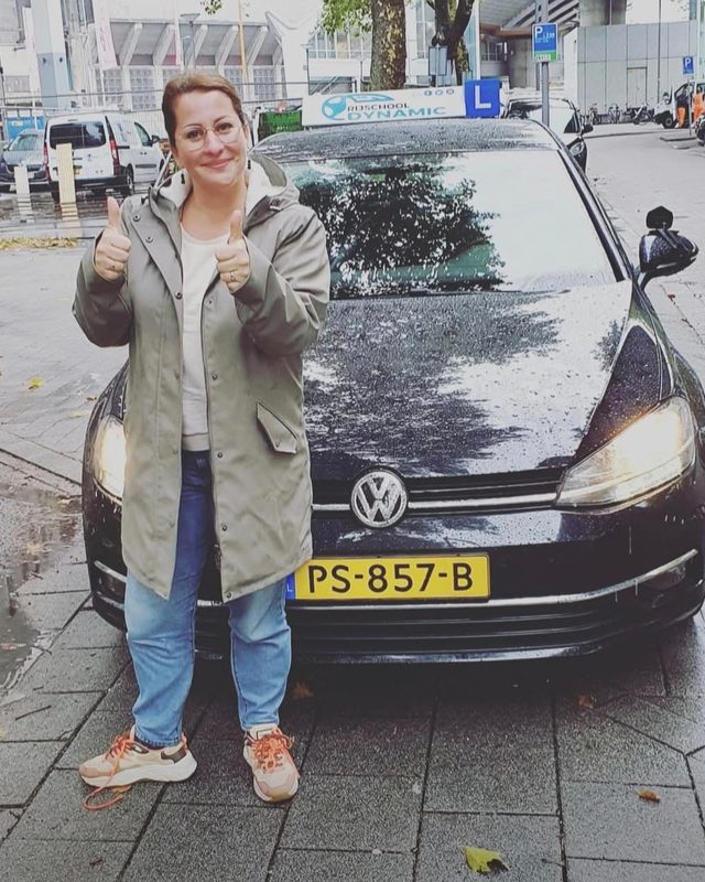 Geslaagde leerling met duim omhoog bij de lesauto van Rijschool Dynamic