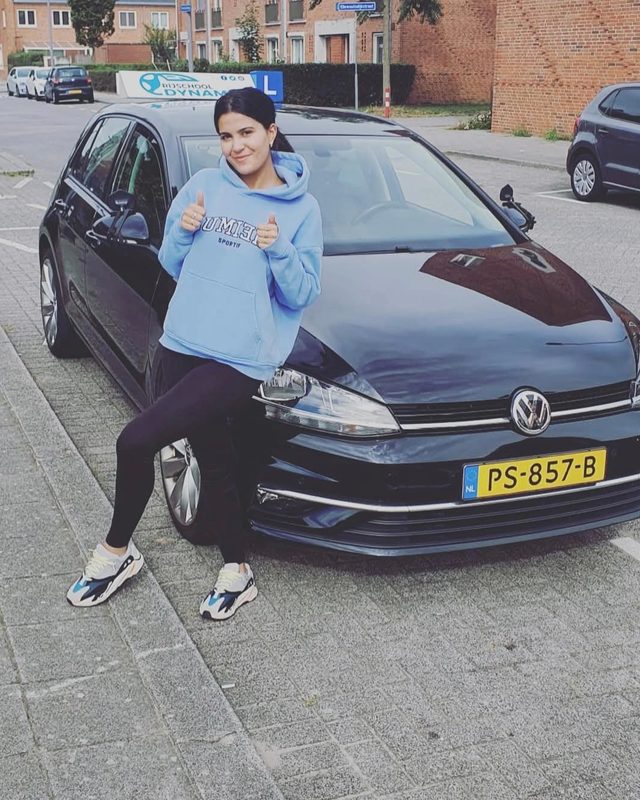 Geslaagde leerling poseert bij de Volkswagen-lesauto